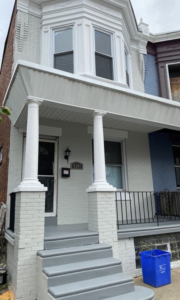 Freshly painted residential entrance with white columns, gray steps, and a blue recycling bin, showcasing expert craftsmanship in commercial painting services.